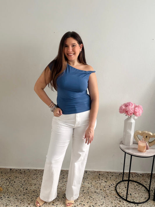 Woman wearing a blue top and white pants standing in a room with a small table and flowers.